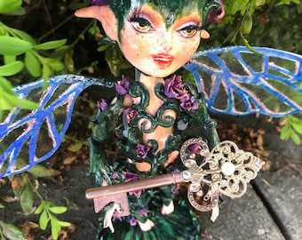 May include: A green fairy figurine with purple flowers in her hair, blue wings, and a gold key. She is wearing a green dress with vines and flowers.