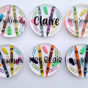 May include: Six clear round coasters with colorful crayons, paper clips, and erasers embedded inside. Each coaster has a teacher's name printed in black lettering: Mrs. Kennedy, Claire, Mrs. Saunders, Mrs. Rodgers, Mrs. Blair, and Mrs. Montes.