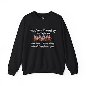 May include: A black long-sleeve sweatshirt featuring a graphic of seven cartoon dwarfs. Above the dwarfs, the text reads "The Seven Dwarfs Of Menopause." Below the dwarfs, the text reads "Itchy, Bitchy, Sweaty, Sleepy, Bloated, Forgetful & Psycho."