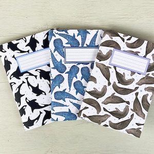 May include: Four different notebooks with white backgrounds and colorful sea creature designs. The notebooks have blank lines for writing names. The designs include orcas, whale sharks, and dolphins.