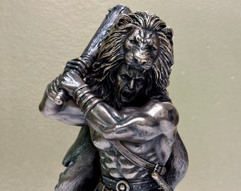 May include: A bronze sculpture of a warrior with a lion's mane, holding a club in his right hand. He is wearing a red loincloth and a leather belt with a metal buckle. The sculpture is detailed and realistic.