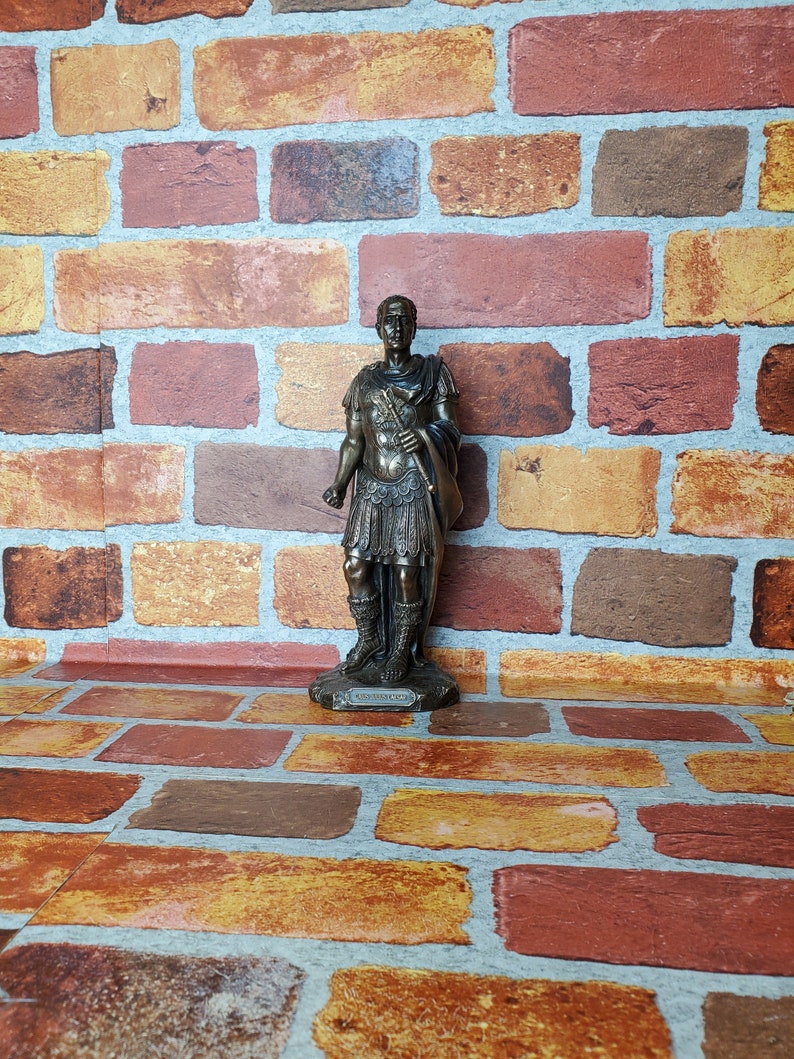 Puede incluir: Estatua de bronce de un soldado romano con toga y espada. La estatua est&aacute; sobre una superficie de ladrillo.