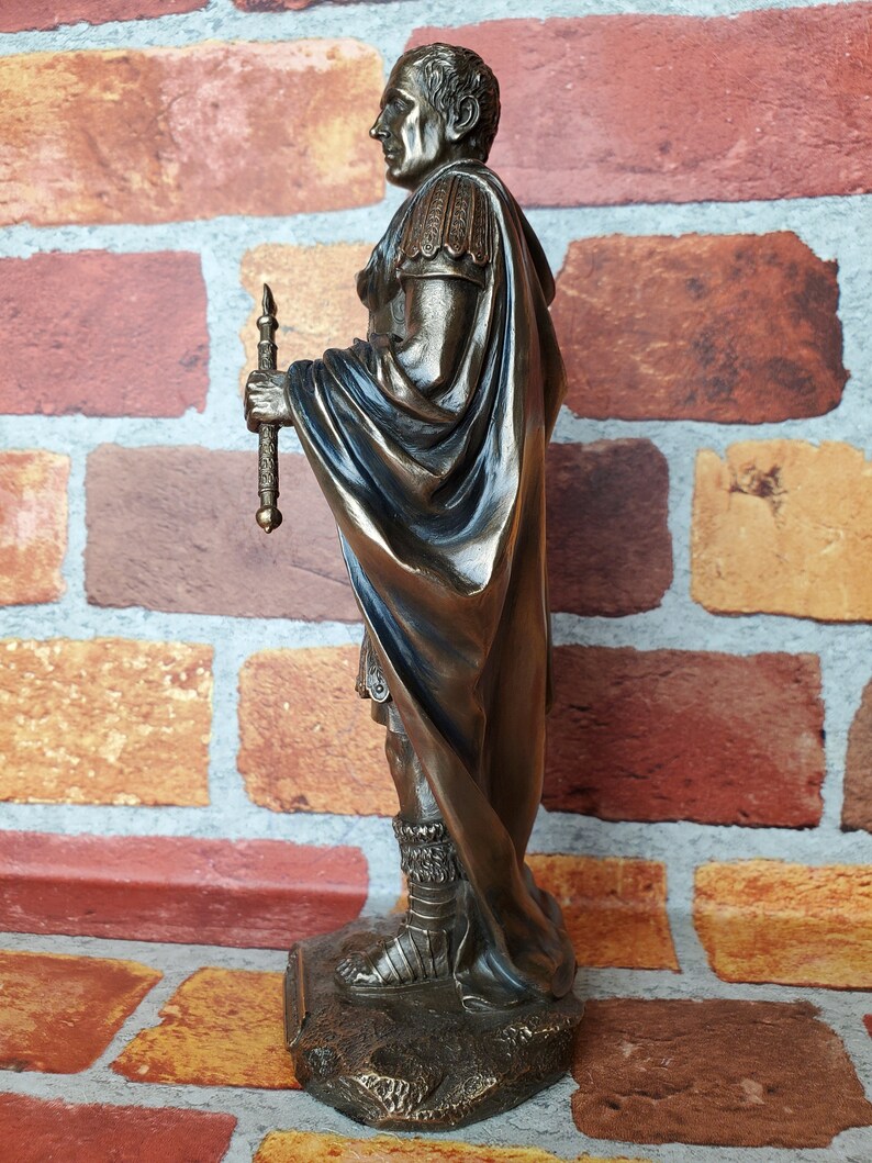 Puede incluir: Estatua de bronce de un soldado romano con toga y sosteniendo una lanza. La estatua est&aacute; de pie sobre una base rocosa.
