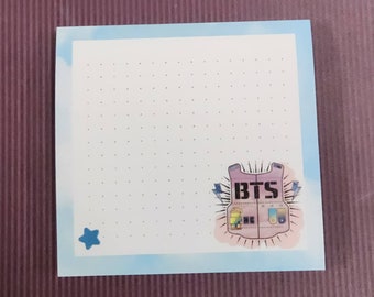 May include: A blue and white notepad with a dotted pattern. The notepad has a sticker of a pink vest with the word "BTS" on it.