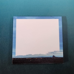 May include: A blank white note card with a blue border. The card is sitting on a green surface.