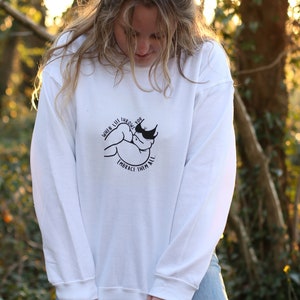 May include: White long-sleeve sweatshirt with a black graphic print of a hand holding a heart with the text "When life throws you, embrace them all."