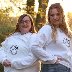May include: Two people wearing white long-sleeved shirts with a black and white graphic of a rhinoceros on the front. The text on the shirt reads "When life throws you curves, embrace them all".