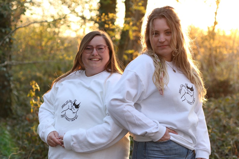 May include: Two people wearing white long-sleeved shirts with a black and white graphic of a rhinoceros on the front. The text on the shirt reads "When life throws you curves, embrace them all".