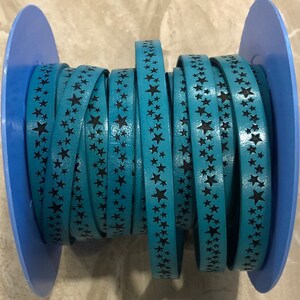 May include: A spool of teal blue leather cord with black star-shaped designs. The cord is wrapped around a blue spool.