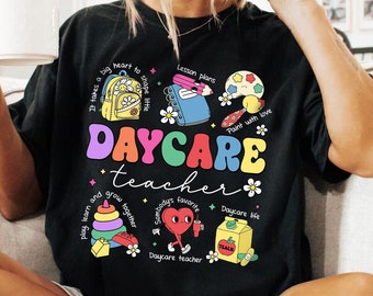 Puede incluir: Camiseta negra con un diseño gráfico colorido que dice "Daycare Teacher". El gráfico incluye imágenes de una mochila, pinceles, un corazón, una caja de jugo y bloques de construcción.