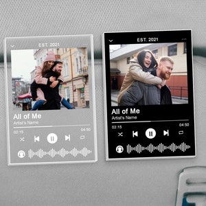 May include: Two black and white digital music player mockups with a photo of a couple in the background. The text on the mockups reads "All of Me" and "Artist's Name". The mockups also include play, pause, and skip buttons, as well as a timer.