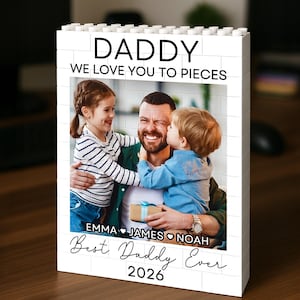 May include: A white rectangular block frame with a brick-like texture featuring a printed photograph of a parent with two children. The text reads DADDY WE LOVE YOU TO PIECES, EMMA, JAMES, NOAH, Best Daddy Ever, and 2026 in black lettering.