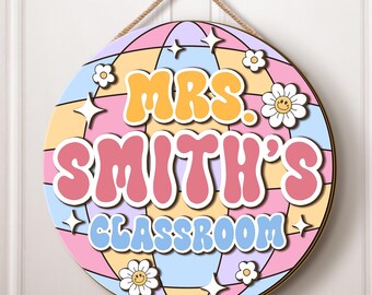 May include: A round classroom door sign with a colorful retro design. The sign features a pink, yellow, and blue globe with white stars and flowers. The text "Mrs. Smith's Classroom" is written in a retro font.