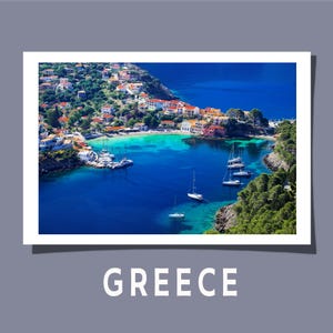 Op de afbeelding: Een schilderachtig luchtfoto van een Griekse kustplaats met kleurrijke gebouwen en boten in het turquoise water. De afbeelding is wit omlijst met het woord "GREECE" in grote witte letters onderaan.
