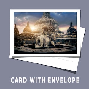 Op de afbeelding: Een witte kaart met een afbeelding van een stenen Boeddha-standbeeld voor een tempelcomplex bij zonsondergang. De tekst "CARD WITH ENVELOPE" staat onderaan afgedrukt.