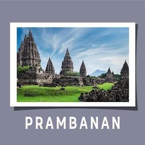 Könnte beinhalten: Eine Fotografie des Prambanan-Tempelkomplexes mit hohen, dunkelgrauen Steintürmen mit detaillierten Schnitzereien vor einem hellblauen Himmel mit leichten Wolken. Die Bauwerke sind von leuchtend grünem Gras und einem fernen Berg umgeben.