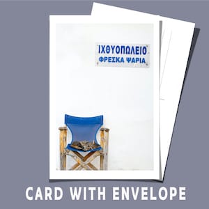 May include: A photograph of a card with an envelope. The card features a blue chair with a sleeping cat in front of a white wall. A blue sign with Greek text is above the chair. The words "CARD WITH ENVELOPE" are at the bottom.