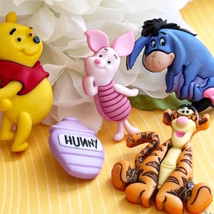 May include: A set of four character-shaped buttons featuring a yellow bear in a red shirt, a small pink pig, a blue donkey, and an orange tiger with black stripes, alongside a purple honey pot button with the word HUNNY printed in black.