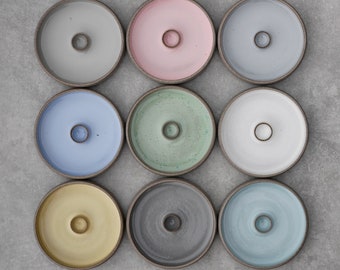 May include: Nine ceramic candle holders in various colors, including light blue, light green, gray, yellow, and pink. Each holder has a round shape with a small hole in the center.