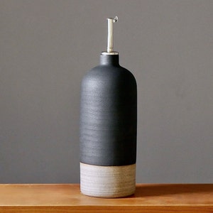 Könnte beinhalten: Schwarze und weiße Keramik-Öl- und Essigflasche mit einem silbernen Ausgießer.