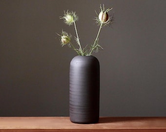 Può includere: Un vaso in ceramica nero con una superficie testurizzata contiene un mazzo di fiori secchi.