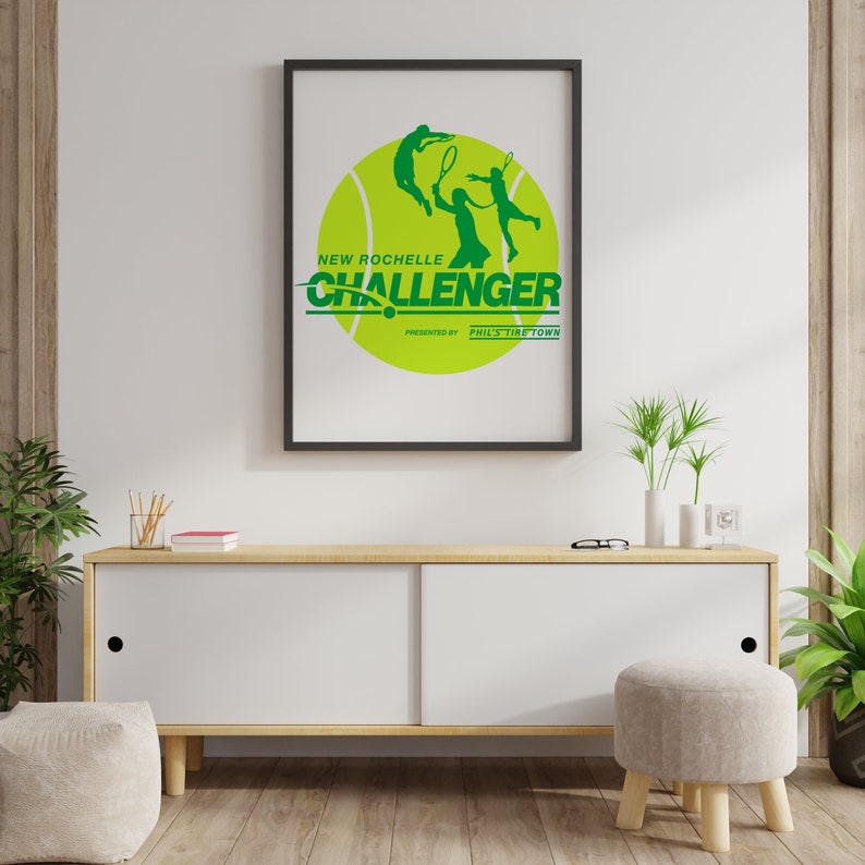 K&ouml;nnte beinhalten: Ein gerahmtes Poster mit einer gr&uuml;nen Tennisballgrafik und dem Text "New Rochelle Challenger" mit den Worten "Presented by Phil's Tire Town" darunter. Das Poster h&auml;ngt an einer wei&szlig;en Wand &uuml;ber einem Holzschrank.
