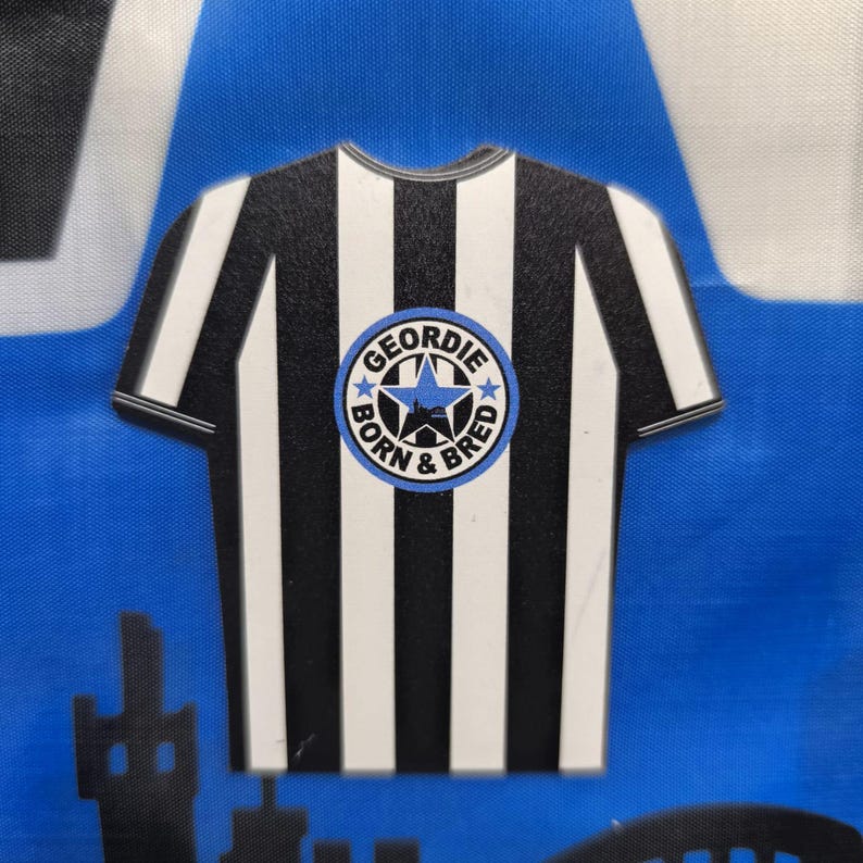 May include: Black and white striped shirt with a blue and white circle logo that says "Geordie Born & Bred" with a star and a city skyline inside the circle.