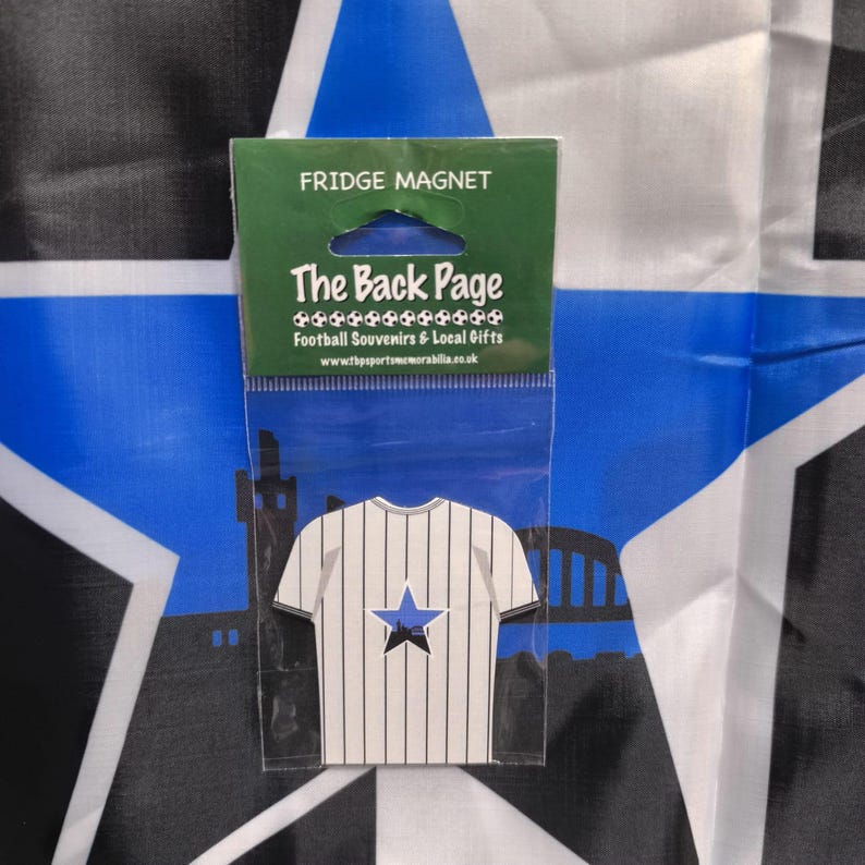 May include: A fridge magnet in a clear plastic sleeve. The magnet is shaped like a white and black striped soccer jersey with a blue star and a black silhouette. The packaging reads "FRIDGE MAGNET" and "The Back Page".