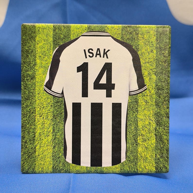 Puede incluir: Una camiseta de f&uacute;tbol a rayas blancas y negras con el nombre "ISAK" y el n&uacute;mero "14" en la espalda. La camiseta est&aacute; sobre un fondo verde y amarillo.