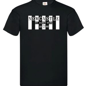 Op de afbeelding: Zwart T-shirt met een witte afbeelding van het logo van de Newcastle United Football Club. Het logo bevat de tekst "NEWCASTLE", "ST. JAMES' PARK" en de jaren "1892".