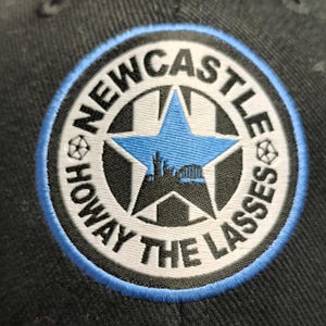 May include: A black and white embroidered patch with a blue star and the text "NEWCASTLE HOWAY THE LASSES" in a circle.