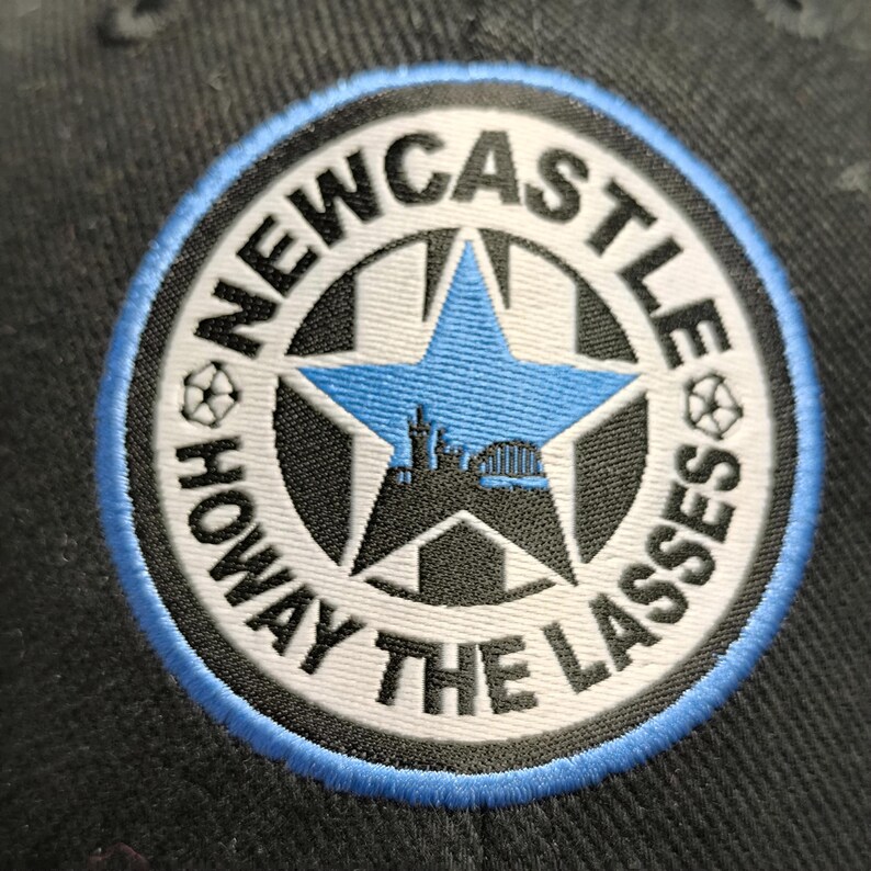 May include: A black and white embroidered patch with a blue star and the text "NEWCASTLE HOWAY THE LASSES" in a circle.