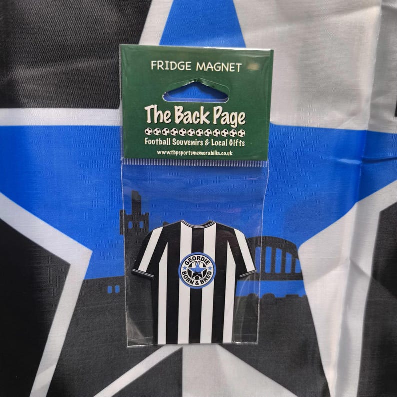May include: A black and white striped fridge magnet shaped like a soccer jersey with a blue circle logo that says "Geordie Born & Bred". The magnet is packaged in a clear plastic bag with a header that says "Fridge Magnet" and "The Back Page Football Souvenirs & Local Gifts".