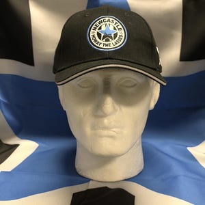 May include: Black baseball cap with a white and blue embroidered logo that says "Newcastle" and "Howay The Lasses".