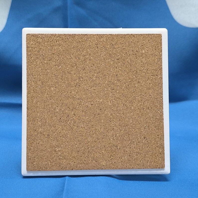 May include: A white square coaster with a cork backing. The coaster is made of a hard material and has a smooth surface.