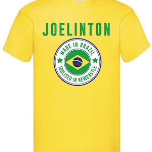 Puede incluir: Camiseta amarilla con el texto "JOELINGTON" y un gr&aacute;fico circular con el texto "MADE IN BRAZIL IDOLISED IN NEWCASTLE" y una bandera brasile&ntilde;a verde, amarilla y azul.