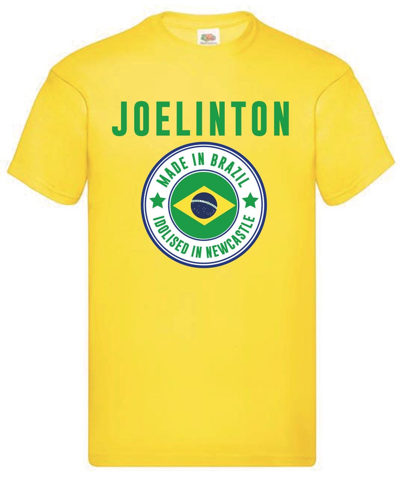 Puede incluir: Camiseta amarilla con el texto "JOELINGTON" y un gr&aacute;fico circular con el texto "MADE IN BRAZIL IDOLISED IN NEWCASTLE" y una bandera brasile&ntilde;a verde, amarilla y azul.