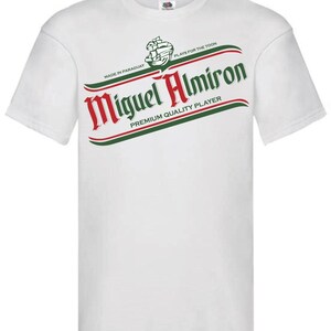 May include: White t-shirt with a green and red graphic of a beer label that says "Miguel Almiron" with the text "Made in Paraguay" and "Plays for the Toon" above the name and "Premium Quality Player" below the name.