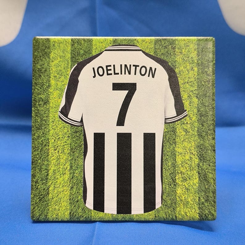 K&ouml;nnte beinhalten: Ein schwarz-wei&szlig;es Fu&szlig;balltrikot mit schwarzen und wei&szlig;en Streifen. Das Trikot tr&auml;gt den Namen "JOELINGTON" und die Nummer "7" auf der R&uuml;ckseite. Das Trikot befindet sich auf einem gr&uuml;n-wei&szlig; gestreiften Hintergrund.