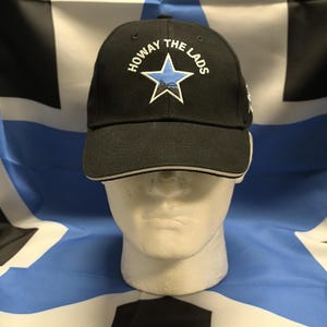 May include: Black baseball cap with a white brim and a blue star with the text "Howay The Lads" embroidered on the front.