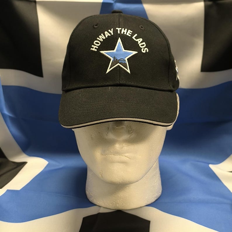 May include: Black baseball cap with a white brim and a blue star with the text "Howay The Lads" embroidered on the front.