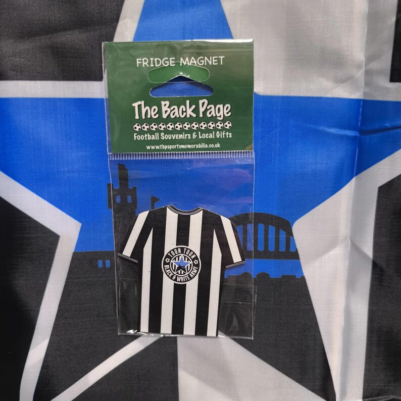 May include: Black and white striped football jersey fridge magnet with a blue star and the words "Town Toon's Black & White Army" in a circle. The magnet is packaged in a clear plastic bag with the words "The Back Page Football Souvenirs & Local Gifts" printed on it.