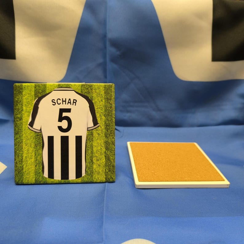 May include: A white and black soccer jersey with the name "SCHAR" and the number "5" on the back. The jersey is on a green and white striped background.