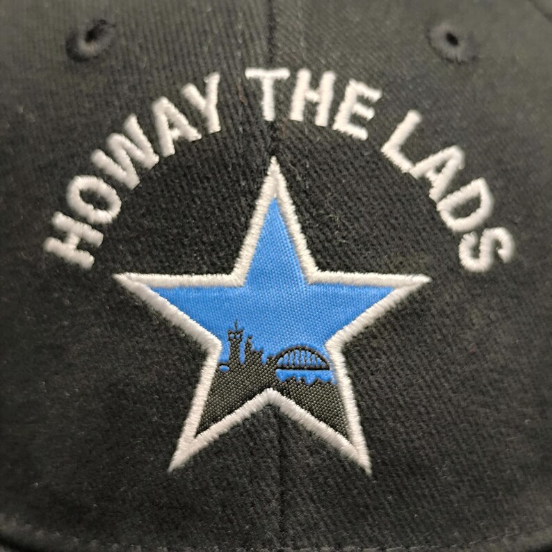 May include: Black baseball cap with white embroidery that reads "Howay The Lads" and a blue star with a city skyline inside.