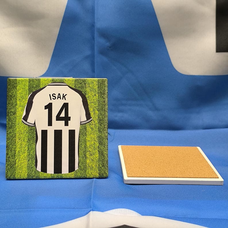 Puede incluir: Una camiseta de f&uacute;tbol a rayas blancas y negras con el nombre "ISAK" y el n&uacute;mero "14" impreso en la espalda. La camiseta est&aacute; sobre un fondo verde y blanco que parece un campo de f&uacute;tbol.