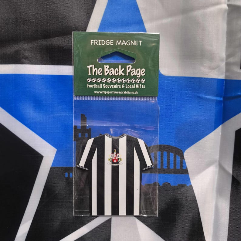 May include: A black and white striped fridge magnet shaped like a soccer jersey with a team crest. The magnet is packaged in a clear plastic bag with the text "The Back Page Football Souvenirs & Local Gifts" and a website address.