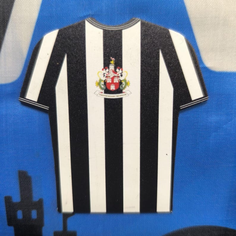 May include: Black and white striped soccer jersey with a team crest featuring a lion and the words "The Pride of the North East".