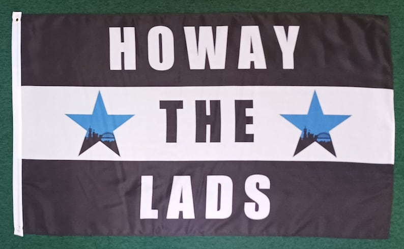 May include: A rectangular flag with the words "HOWAY THE LADS" in large white capital letters. The flag has a black top and bottom with a white stripe in the middle. Two blue stars with a city silhouette are on the white stripe.