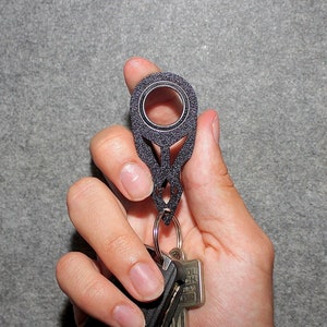 May include: A black key chain with a ring and a small hole in the center. The key chain is attached to a set of keys.
