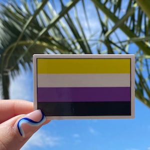 May include: A sticker with the non-binary pride flag. The flag has five horizontal stripes: yellow, white, purple, black, and white.